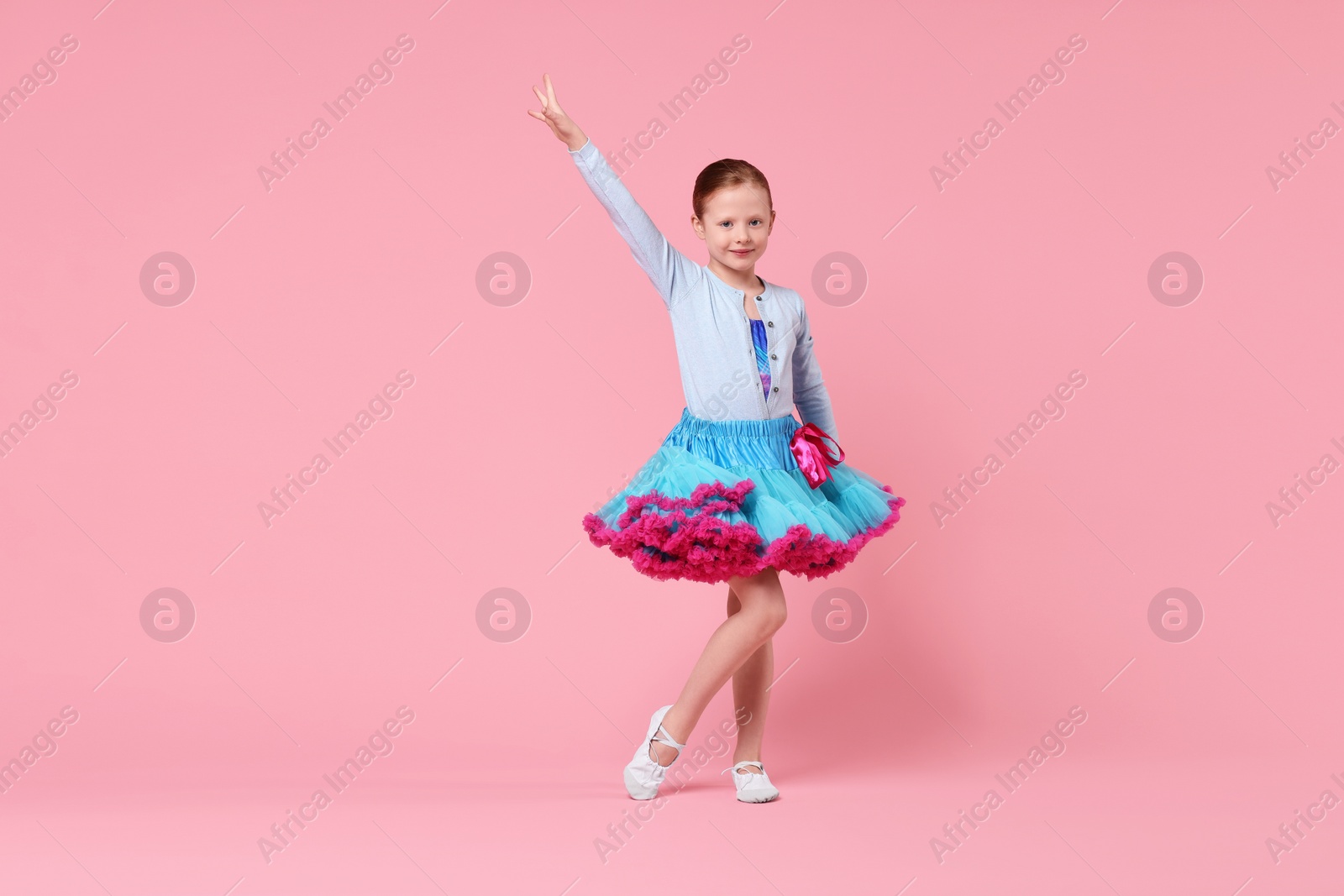 Photo of Cute little girl dancing on pink background