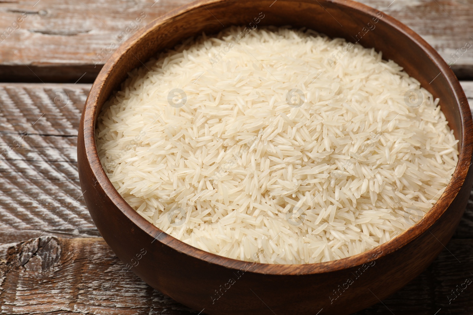 Photo of Raw basmati rice in bowl on wooden table, closeup