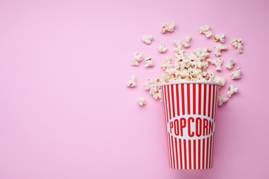 Bucket of tasty popcorn on pink background, flat lay. Space for text