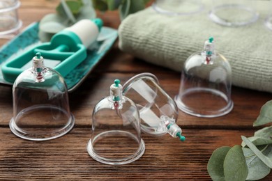 Photo of Cupping therapy. Plastic cups and eucalyptus leaves on wooden table