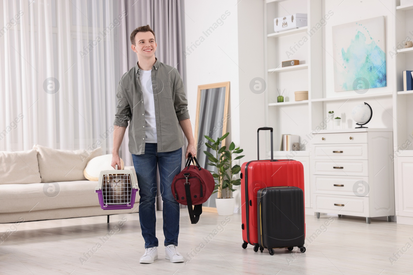 Photo of Travel with pet. Man holding carrier with cute cat and bag at home