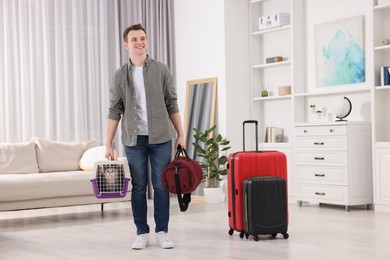 Travel with pet. Man holding carrier with cute cat and bag at home