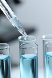 Dripping liquid from pipette into test tube on blurred background, closeup