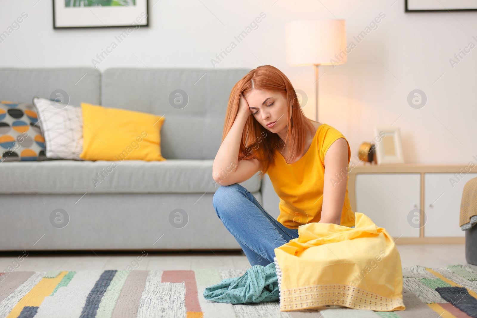 Photo of Tired housewife with laundry sitting on floor at home