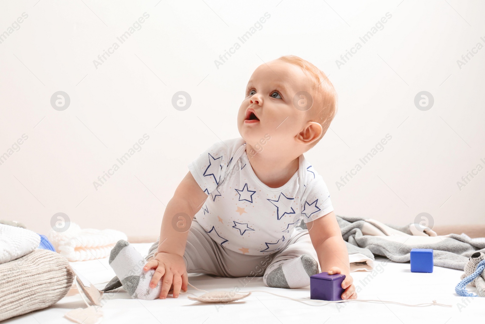 Photo of Little boy in cute clothes sitting on floor against light background. Baby accessories
