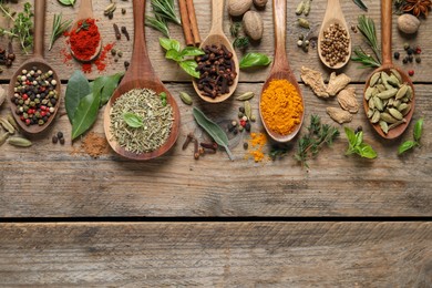 Photo of Different herbs and spices with spoons on wooden table, flat lay. Space for text