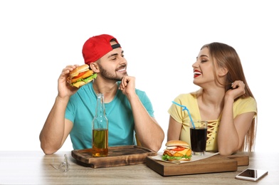 Happy couple having lunch with burgers at table on white background