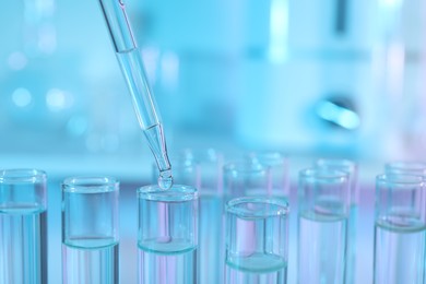 Dripping liquid from pipette into test tube on light blue background, closeup