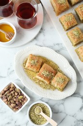 Photo of Delicious fresh baklava with chopped nuts and honey served on white marble table, flat lay. Eastern sweets