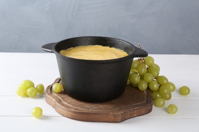 Photo of Fondue with tasty melted cheese and grapes on white wooden table