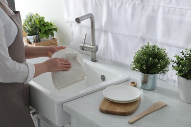 Photo of Woman wiping plate with towel above sink in kitchen, closeup