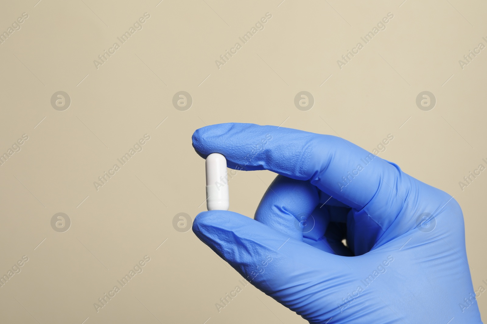 Photo of Doctor holding pill on beige background, closeup