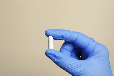 Doctor holding pill on beige background, closeup