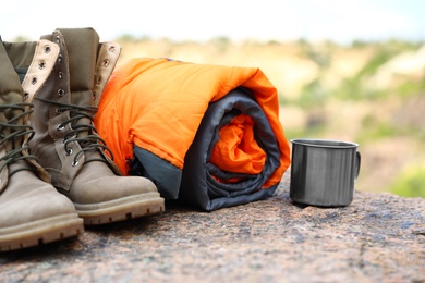 Sleeping bag, cup and boots outdoors on sunny day