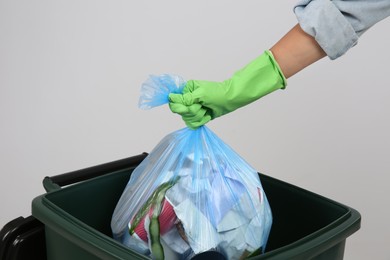 Photo of Woman throwing garbage bag into bin on light background, closeup