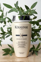 Photo of MYKOLAIV, UKRAINE - SEPTEMBER 07, 2021: Kerastase shampoo and green branches on wooden table. Hair care cosmetic product