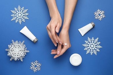 Woman applying cream onto hand on blue background, top view