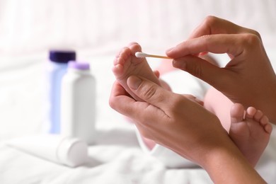 Photo of Mother cleaning baby's foot with cotton bud on bed, closeup