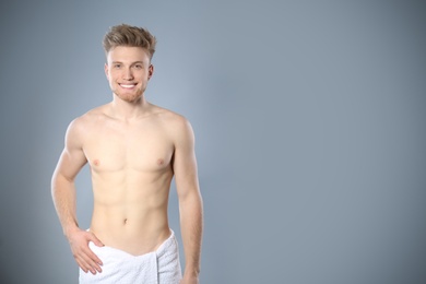 Photo of Portrait of young man with slim body in towel on grey background. Space for text