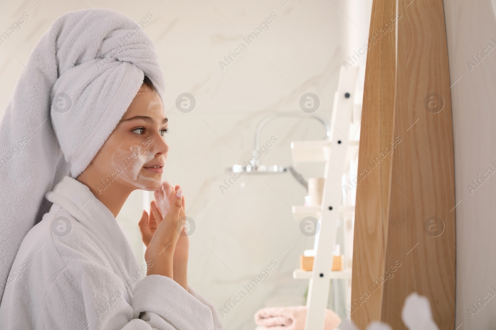 Photo of Beautiful teenage girl applying cleansing foam onto face in bathroom. Skin care cosmetic