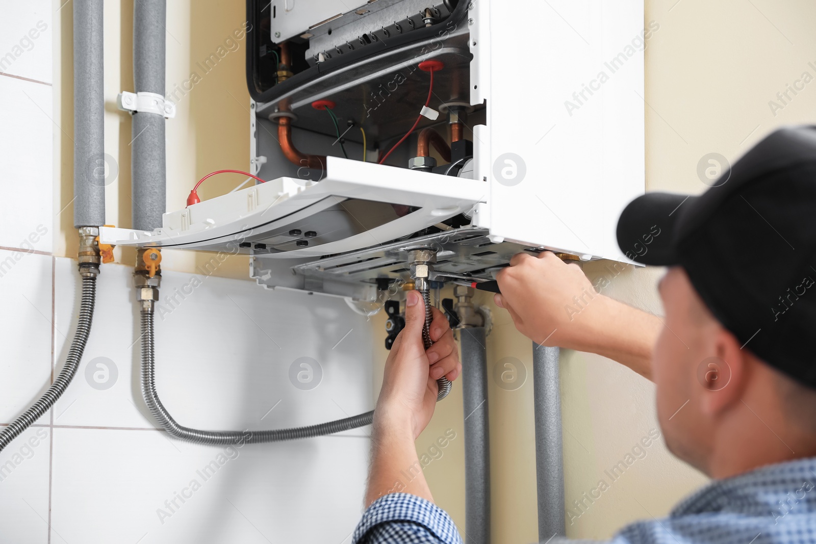 Photo of Man repairing gas boiler with waterpump plier indoors, closeup