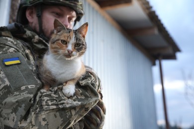 Photo of Ukrainian soldier with stray cat outdoors, closeup. Space for text