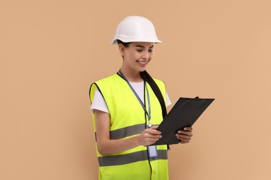 Photo of Engineer in hard hat holding clipboard on beige background