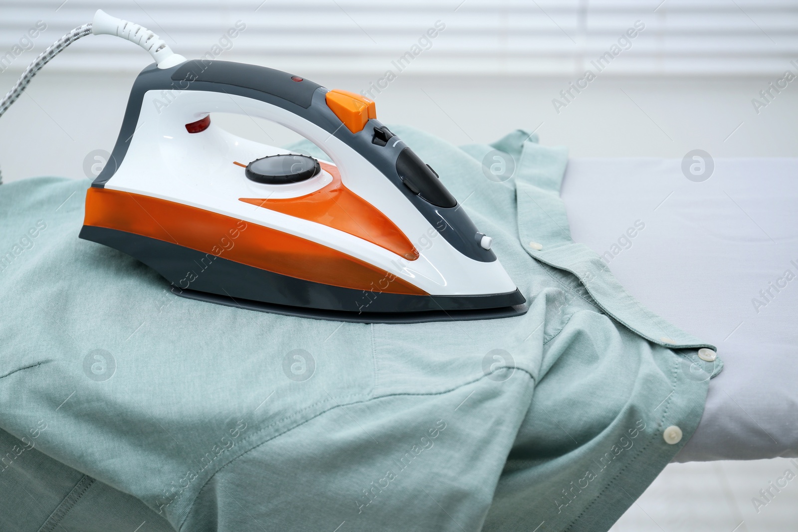 Photo of Modern iron and clean shirt on board indoors