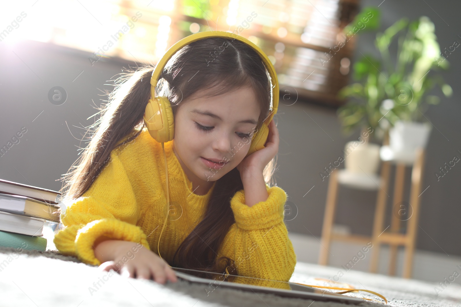 Photo of Cute little girl with headphones and tablet listening to audiobook at home