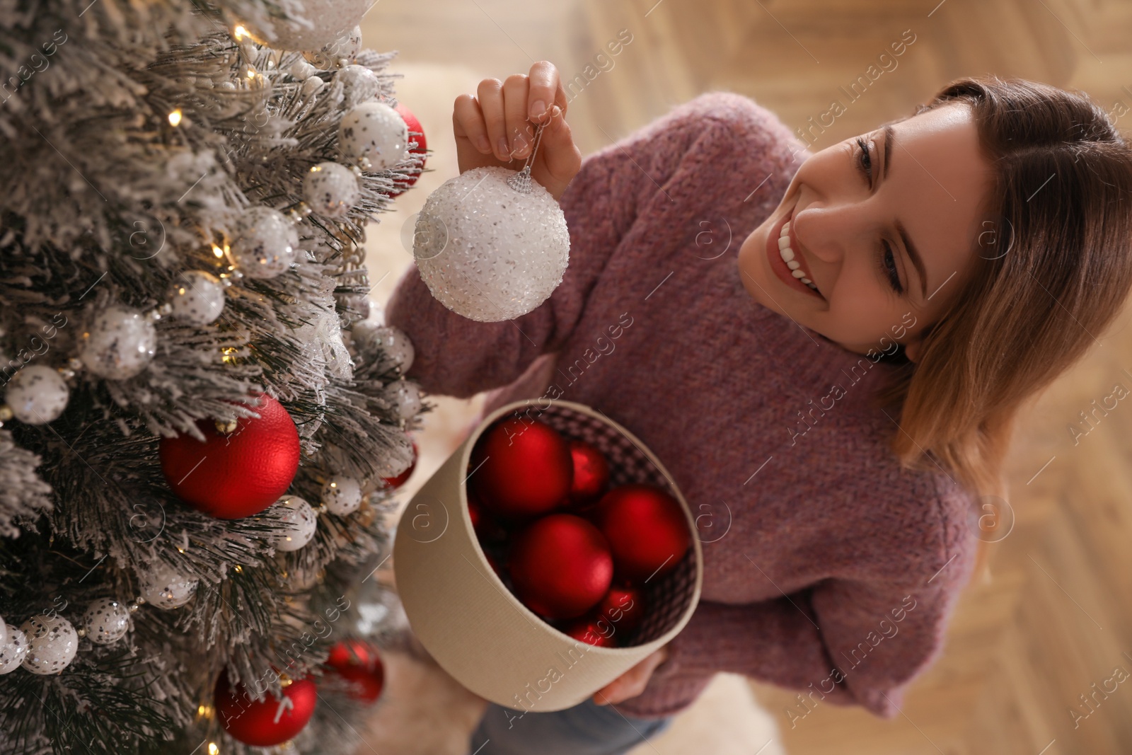 Photo of Young woman decorating Christmas tree at home, above view