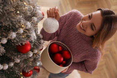 Photo of Young woman decorating Christmas tree at home, above view