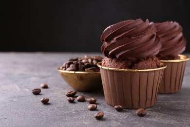 Photo of Delicious chocolate cupcakes and coffee beans on grey textured table, closeup. Space for text