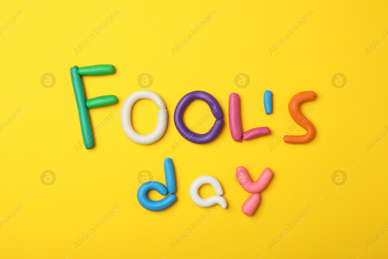 Photo of Words FOOL'S DAY made with clay on yellow background, flat lay. April holiday