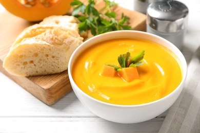 Photo of Bowl with delicious pumpkin cream soup and bread on wooden table