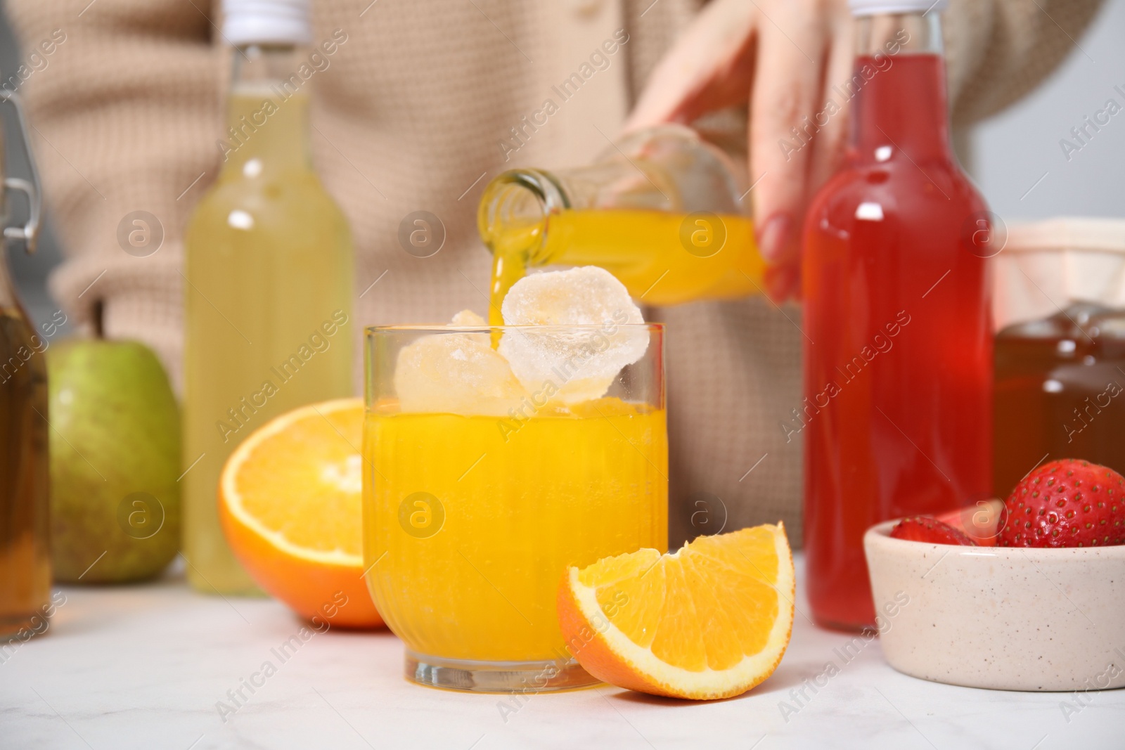 Photo of Woman pouring tasty kombucha into glass with ice at white table, closeup