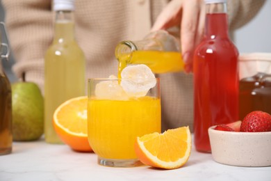 Woman pouring tasty kombucha into glass with ice at white table, closeup