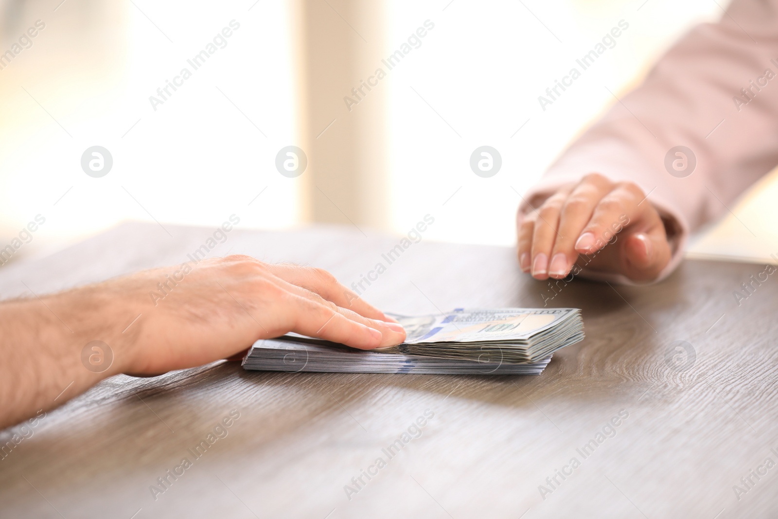 Photo of Man giving dollar bills to businesswoman at wooden table, closeup