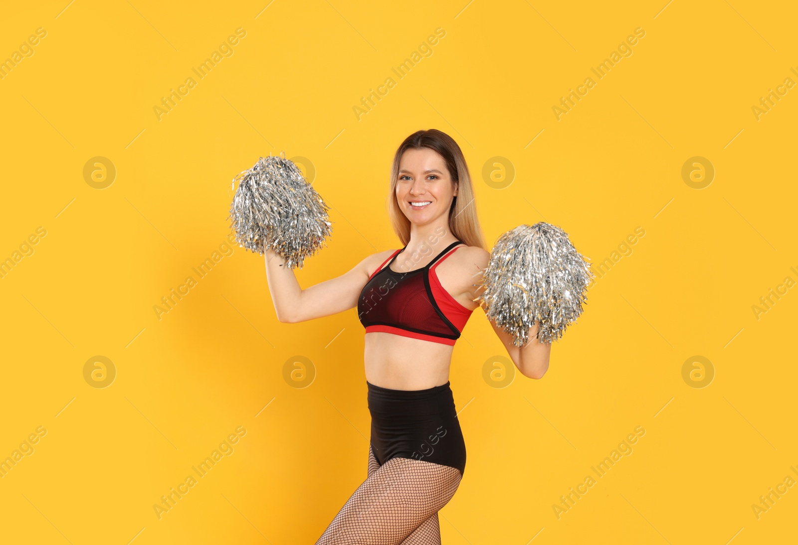 Photo of Beautiful cheerleader in costume holding pom poms on yellow background
