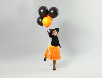 Cute little girl with balloons wearing Halloween costume on grey background