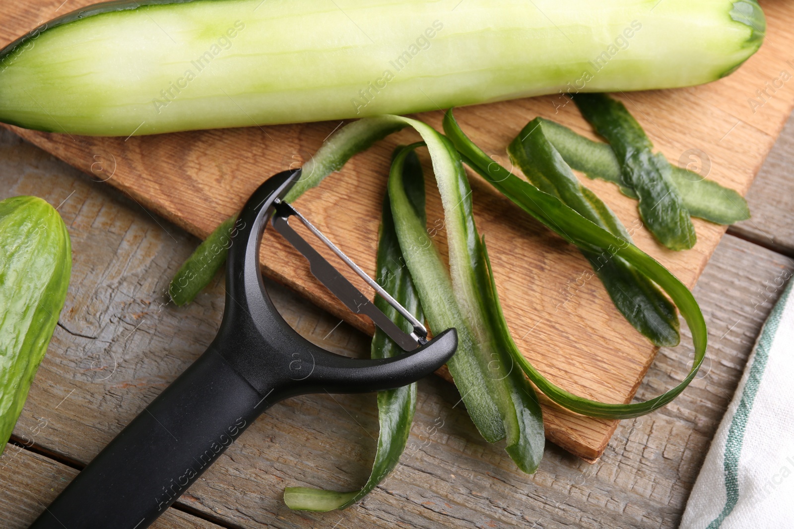 Photo of Fresh cucumber, peels and peeler at wooden table, top view