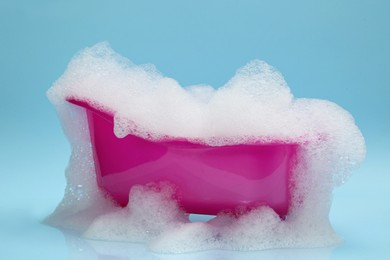 Photo of Toy bathtub overflowing with foam on light blue background