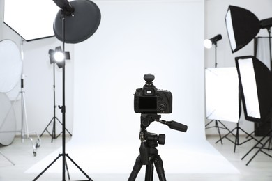 Tripod with camera and professional lighting equipment in modern photo studio