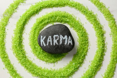 Photo of Stone with word Karma and circle made of light green sea salt on white marble table, top view