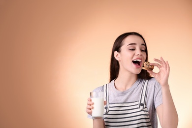 Beautiful young woman drinking milk with cookies on color background