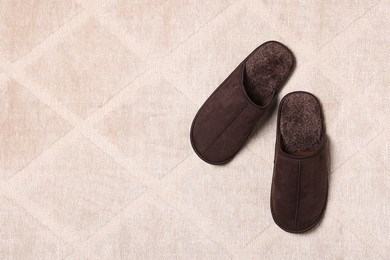 Photo of Brown slippers on soft carpet, top view. Space for text