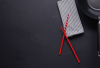 Photo of Empty iron wok and chopsticks on black table, flat lay. Space for text