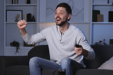 Emotional man watching TV on sofa at home