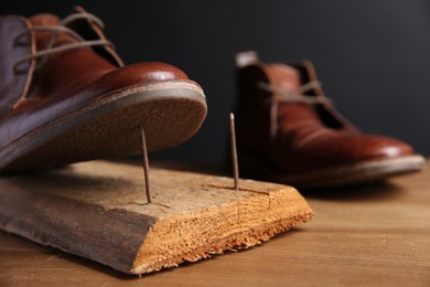 Metal nails in wooden plank and shoes on table