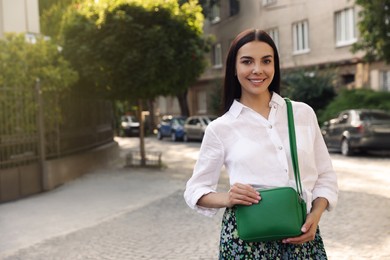 Beautiful young woman with stylish bag on city street, space for text