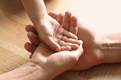 Happy family holding hands on wooden background, closeup